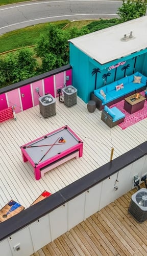 Aerial view of rooftop with pink pool table, teal lounge area, and string lights