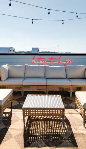 Rooftop terrace with rattan seating, string lights, and boot scootin boogie neon sign